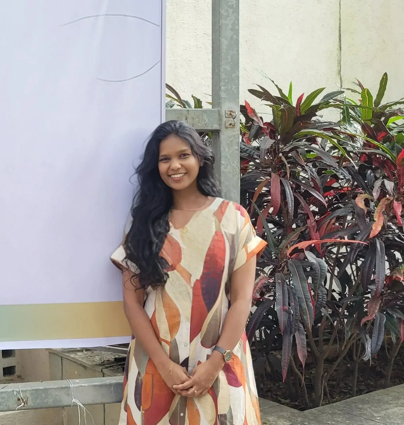Reethika smiling, standing beside a large blank poster